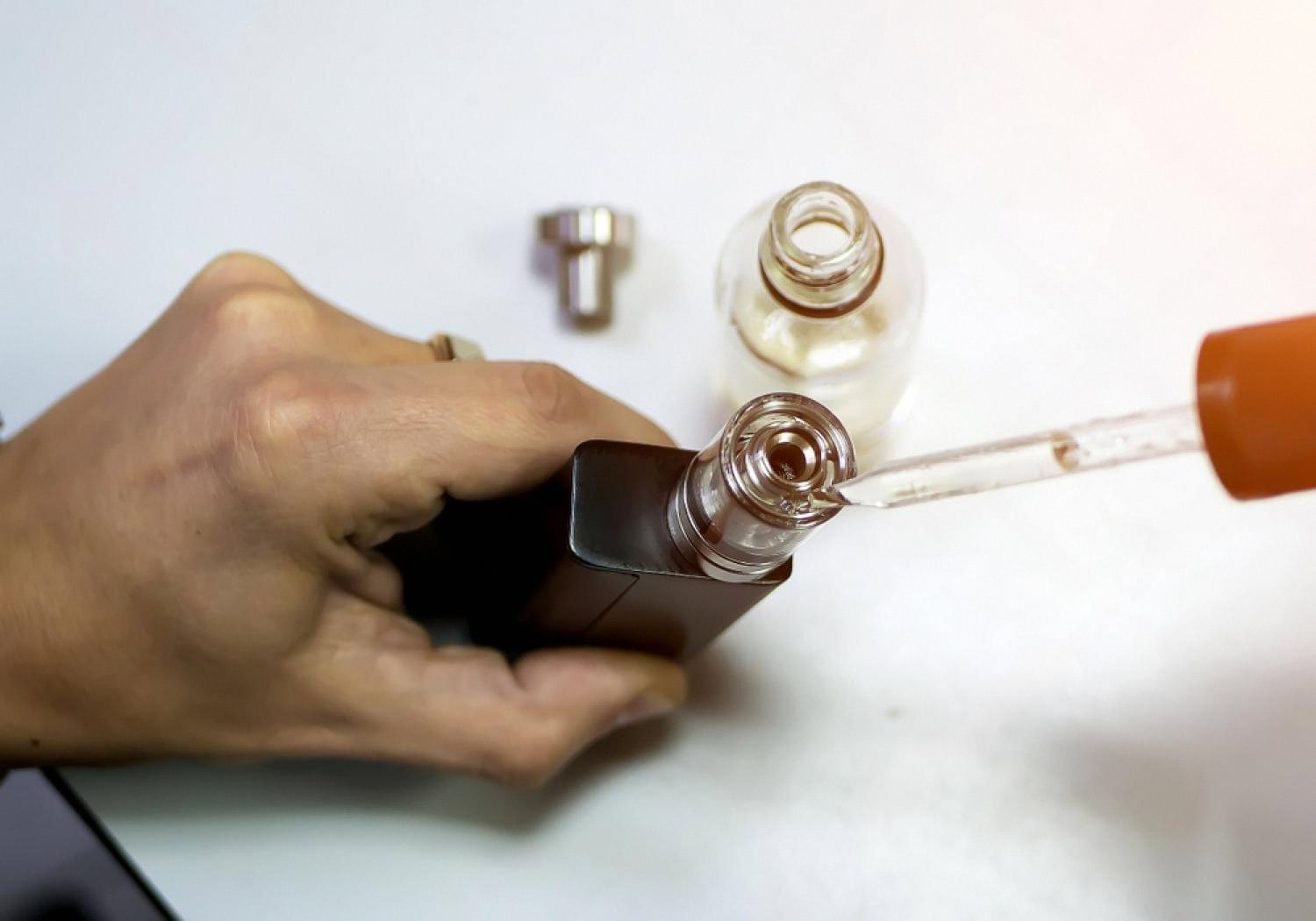 Person refilling a pod vape with e-liquid using a dropper bottle