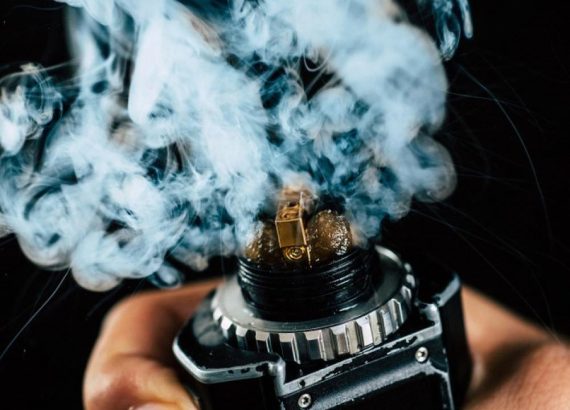 Hand holding a black box mod vape device with a thick cloud of vapour in the UAE